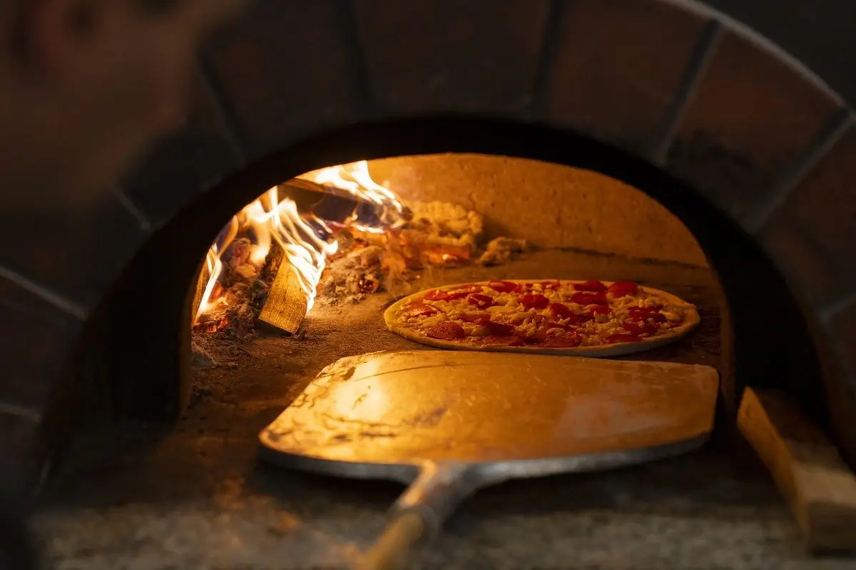 A wide shot of the glowing brick pizza oven, the heart of the kitchen.